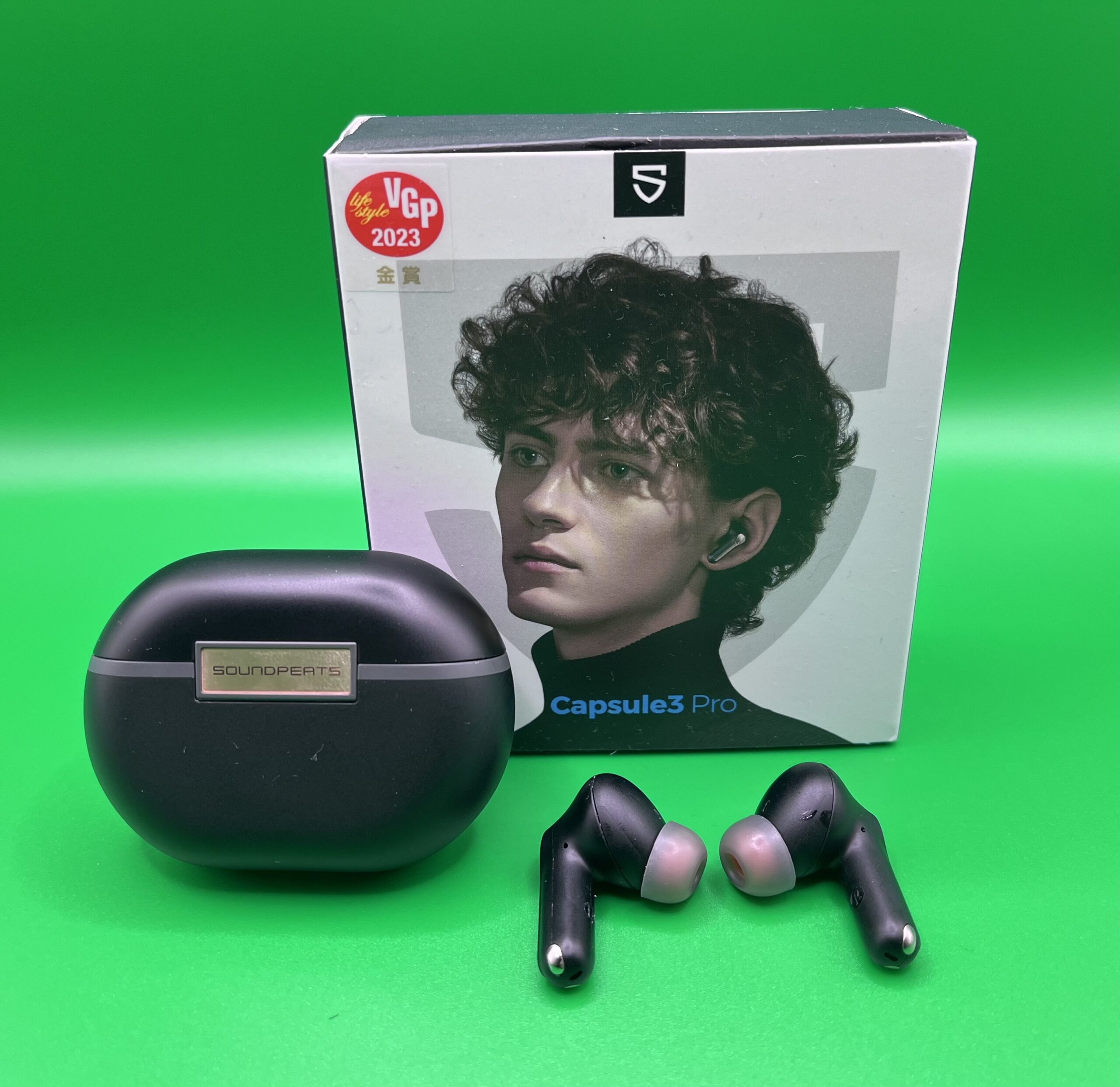 An image of headphones with their box on a green background